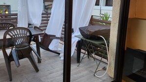 A balcony with a table and chairs, a white curtain, and a view of buildings and a clear sky. - Maison 6 à 8 Personnes Entre Mer et Pic St Loup (Montferrier-sur-Lez)