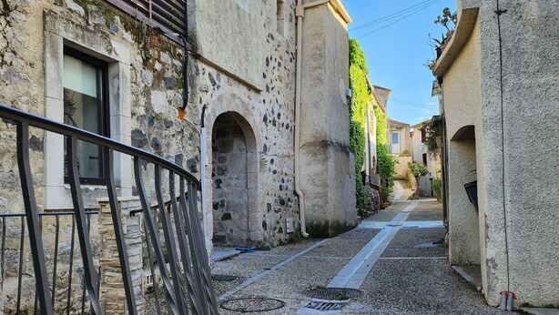 A narrow alleyway with stone buildings, a metal railing, and a clear sky. - Maison 6 à 8 Personnes Entre Mer et Pic St Loup (Montferrier-sur-Lez)