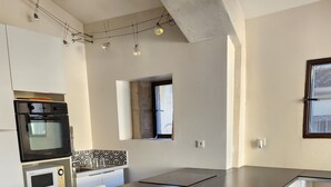 A modern kitchen with a large table, white chairs, a built-in oven, and a microwave. - Maison 6 à 8 Personnes Entre Mer et Pic St Loup (Montferrier-sur-Lez)