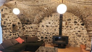 A cozy room with a stone wall, a black sofa, a glass-top coffee table, and a wood-burning stove. - Maison 6 à 8 Personnes Entre Mer et Pic St Loup (Montferrier-sur-Lez)