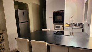 A compact kitchen with a black countertop, white cabinets, a built-in oven, microwave, and a small sink with a yellow towel. - Maison 6 à 8 Personnes Entre Mer et Pic St Loup (Montferrier-sur-Lez)