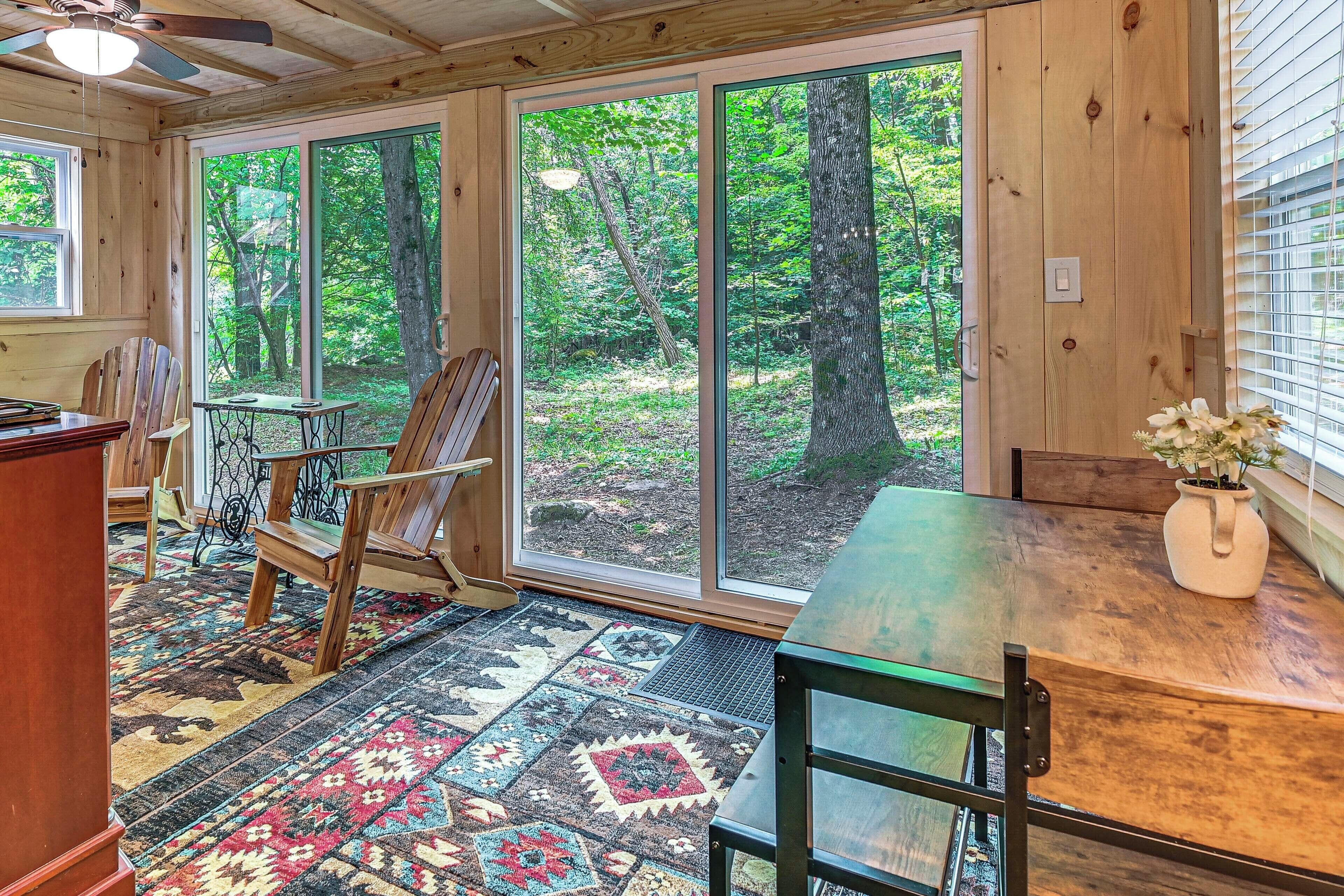 A cozy cabin interior with large windows, a wooden floor, and rustic furniture.