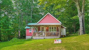A red cabin with a porch, surrounded by a forest.