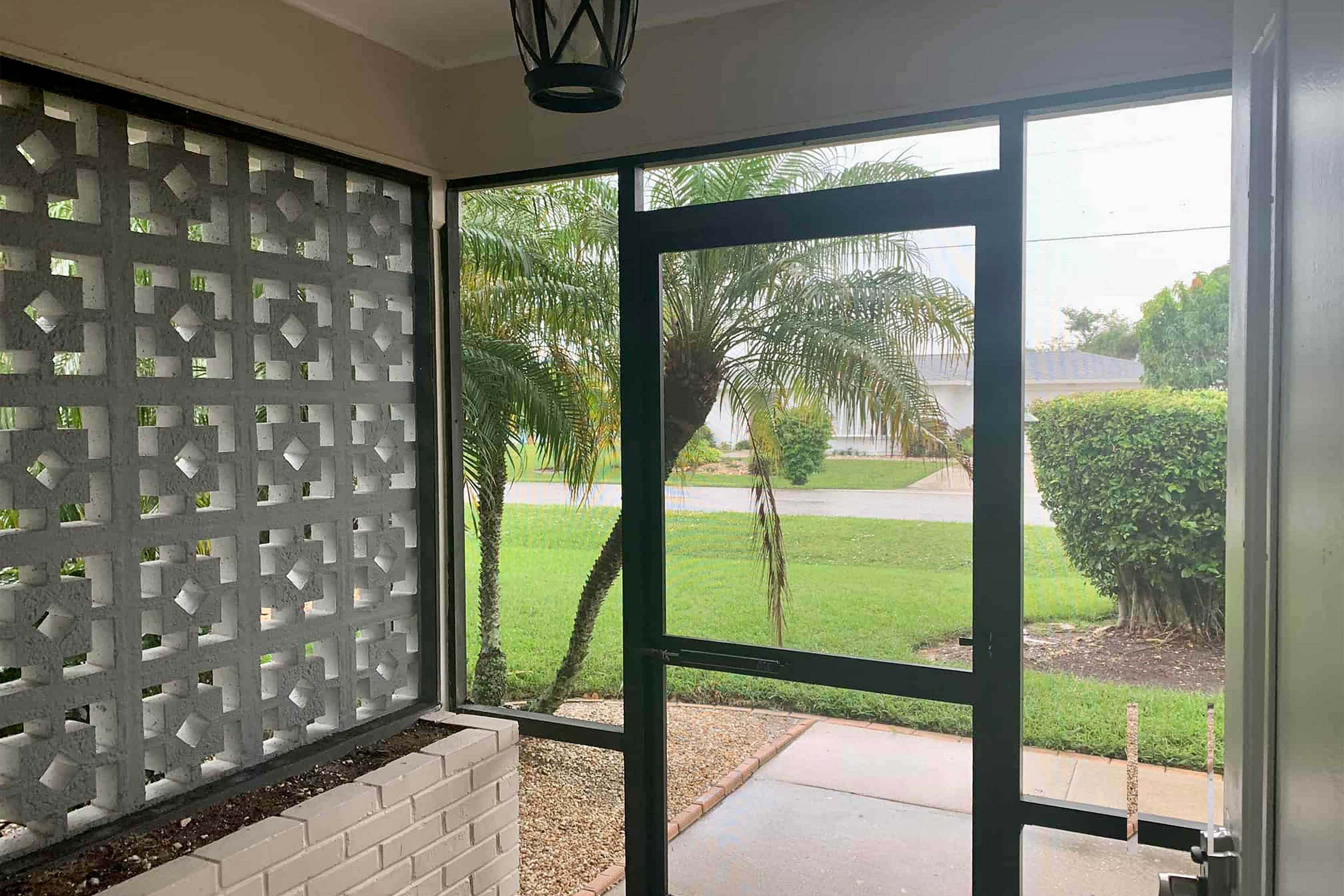 A room with a large glass door leading to a view of a well-maintained lawn and palm trees.
