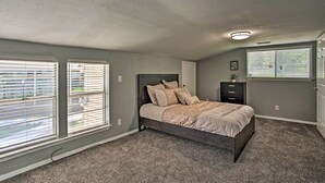 Ein Schlafzimmer mit einem Bett, zwei Fenstern mit Jalousien, einer Kommode und einer Deckenleuchte.
