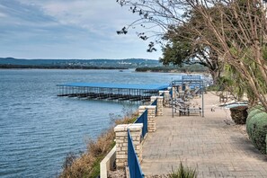 A waterfront walkway with a stone railing, benches, and a covered area.