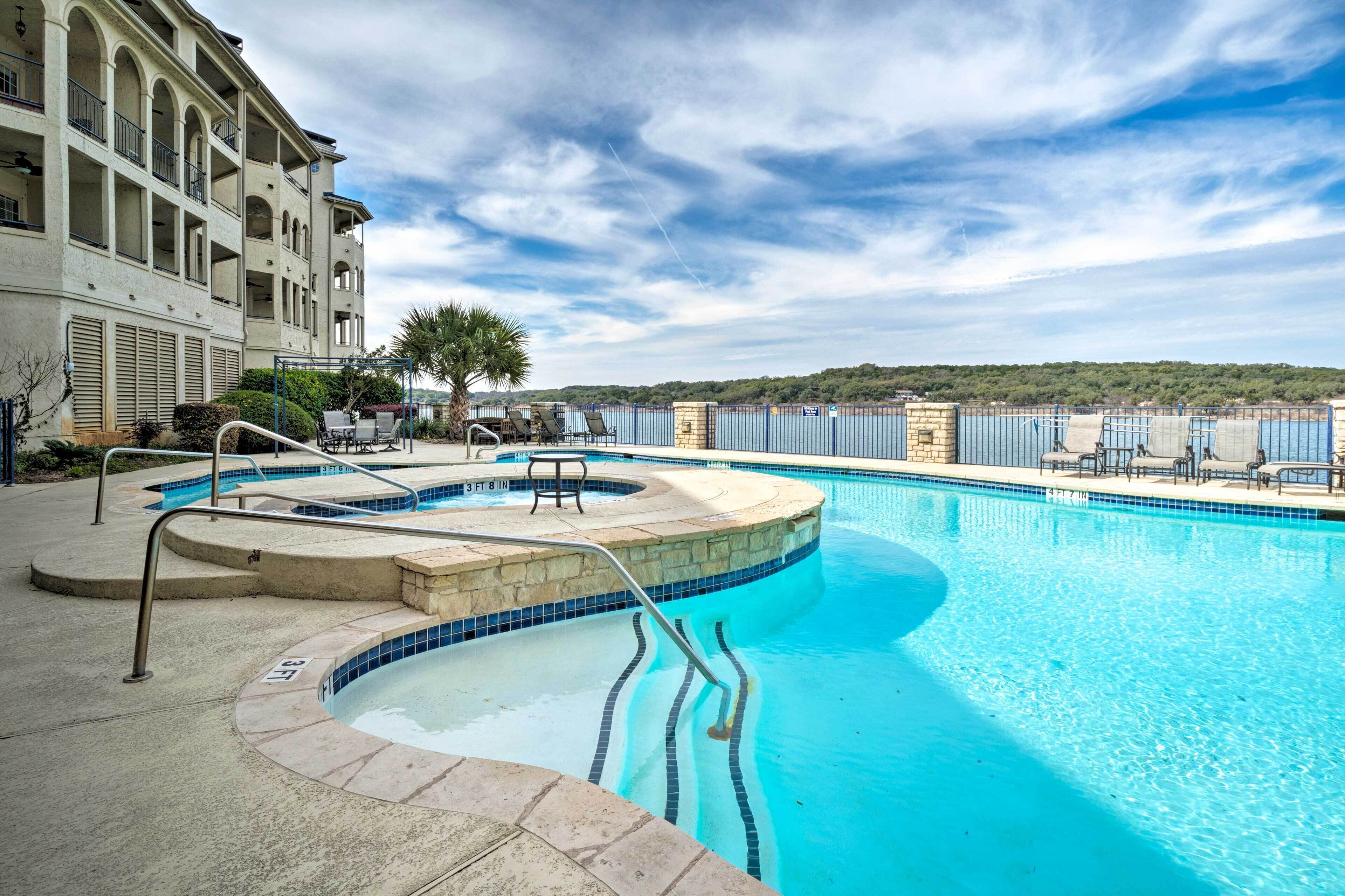 A swimming pool with a view of the sea, a palm tree, and a building with balconies.