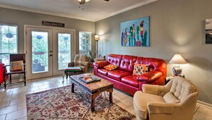A living room with a red leather sofa, a beige armchair, and a coffee table. There is a ceiling fan, a painting on the wall, and a door with a sign. - Lakefront Lago Vista Condo w/ Resort Amenities! (Leander)