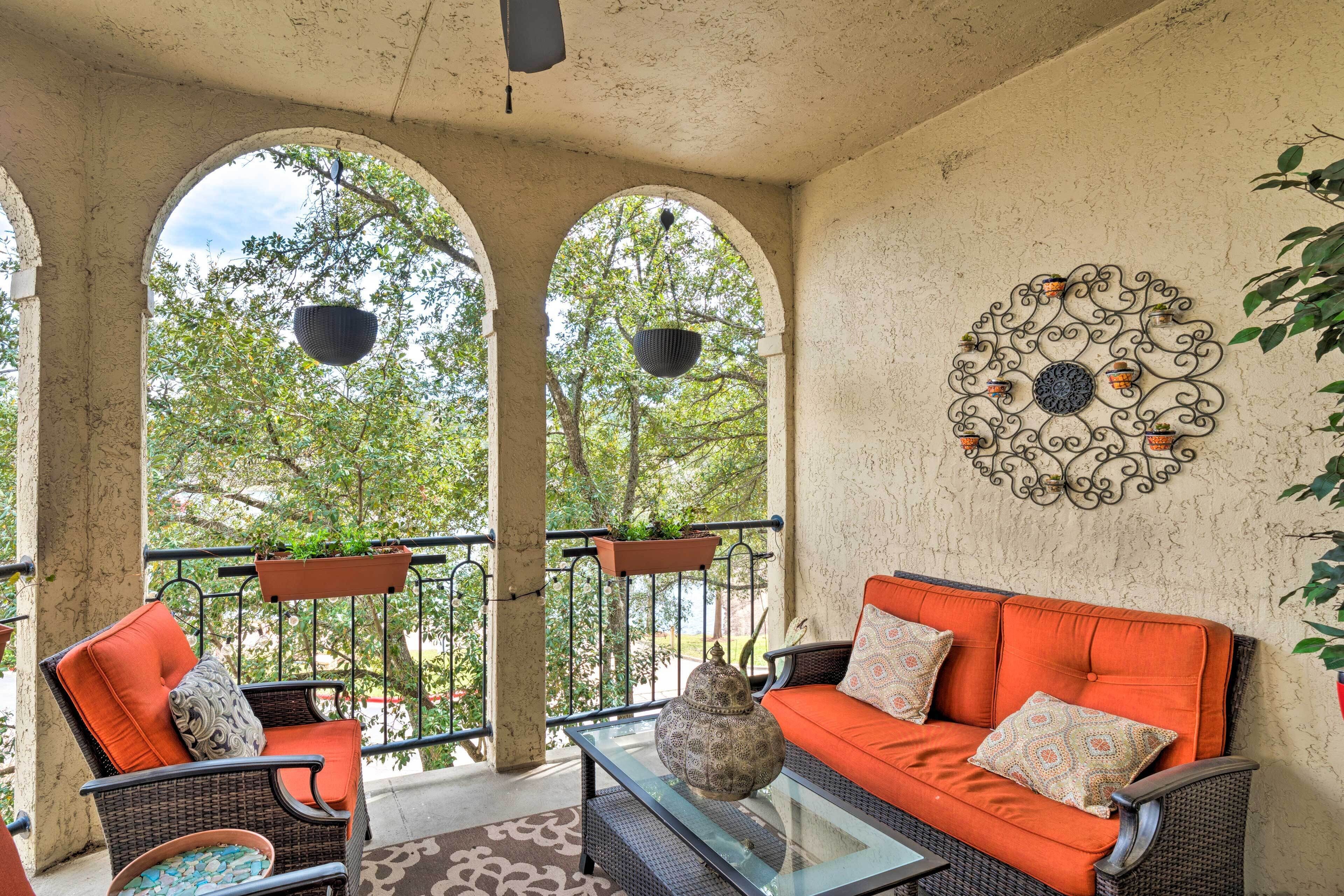 An outdoor seating area with wicker furniture, orange cushions, and hanging planters.