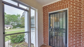 Een kamer met een bakstenen muur, een glazen deur met een metalen hekwerk, en uitzicht op een woonstraat.