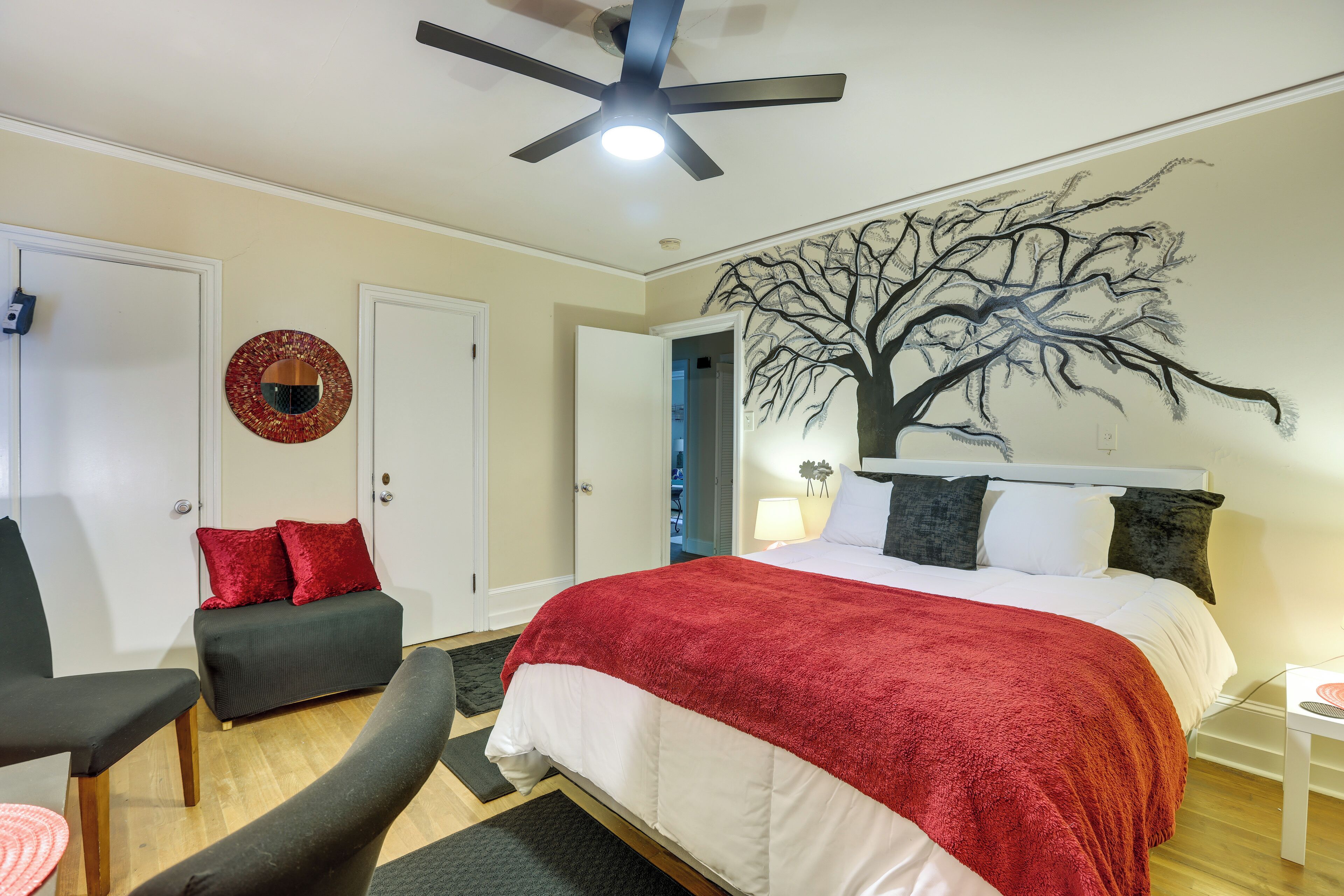 A bedroom with a bed, a ceiling fan, a wall mural, a desk, and a chair.