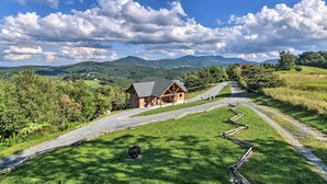 A rustic cabin with a stone foundation and wooden beams, surrounded by lush greenery and a winding road. - 'high Gravity' Banner Elk Custom Chalet w/ Views! (Banner Elk)