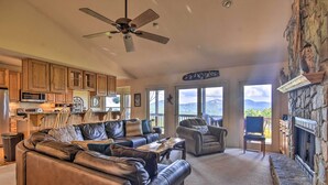 A spacious living room with a leather sofa, a stone fireplace, and a view of mountains through large windows. - 'high Gravity' Banner Elk Custom Chalet w/ Views! (Banner Elk)