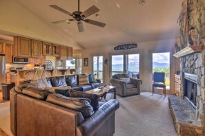 A spacious living room with a leather sofa, a stone fireplace, and a view of mountains through large windows. - 'high Gravity' Banner Elk Custom Chalet w/ Views! (Banner Elk)