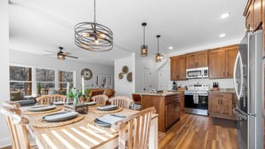 A modern kitchen with wooden cabinets, stainless steel appliances, and a dining area with a wooden table and chairs. - Charming Murphy House With Deck & River Views! (Murphy)