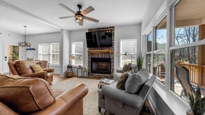 A living room with leather sofas, a fireplace, and a large window overlooking a deck. - Charming Murphy House With Deck & River Views! (Murphy)