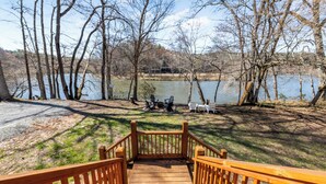 A wooden deck leading to a lakeside area with chairs and tables. - Charming Murphy House With Deck & River Views! (Murphy)