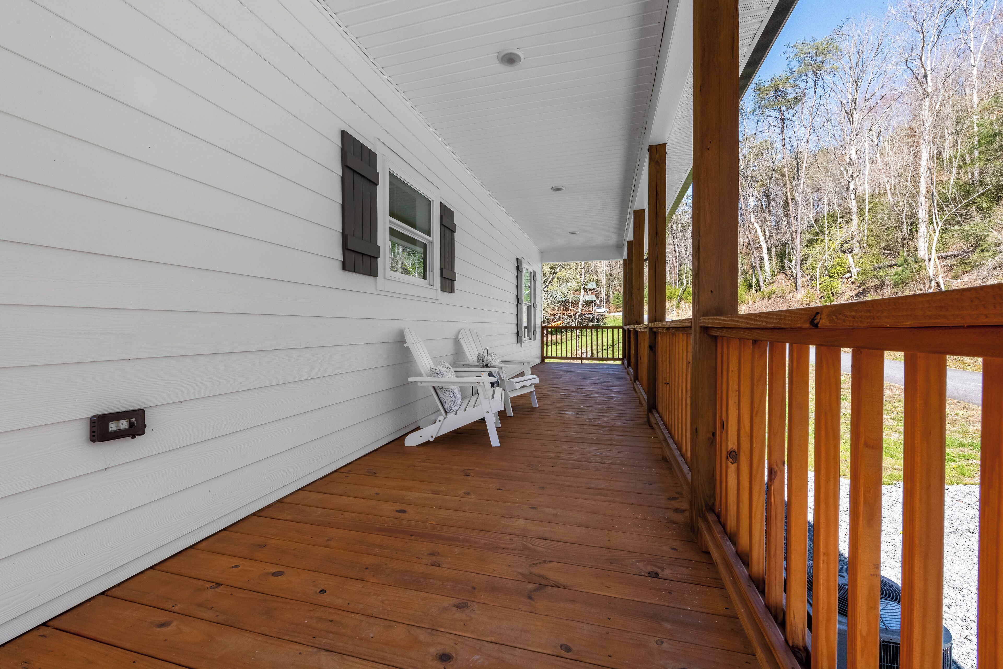 Une véranda couverte avec des balustrades en bois, un revêtement extérieur blanc et une rangée de chaises blanches.