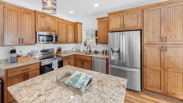 A modern kitchen with wooden cabinets, stainless steel appliances, granite countertops, and pendant lighting. - Charming Murphy House With Deck & River Views! (Murphy)