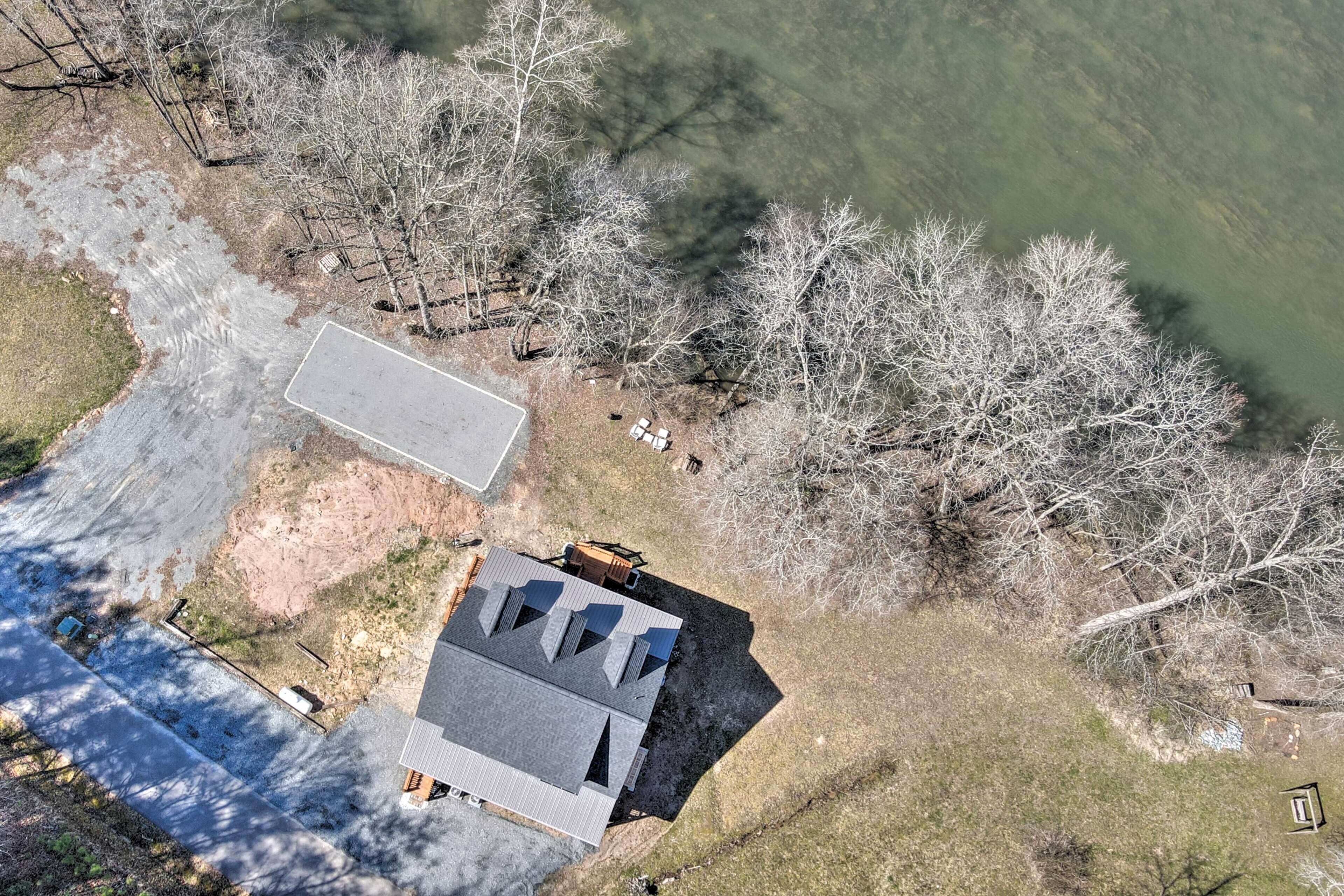 An aerial view of a house with a large driveway, a fenced yard, and a body of water nearby.