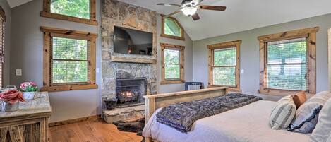 A bedroom with a stone fireplace, wooden beams, a bed, and large windows.