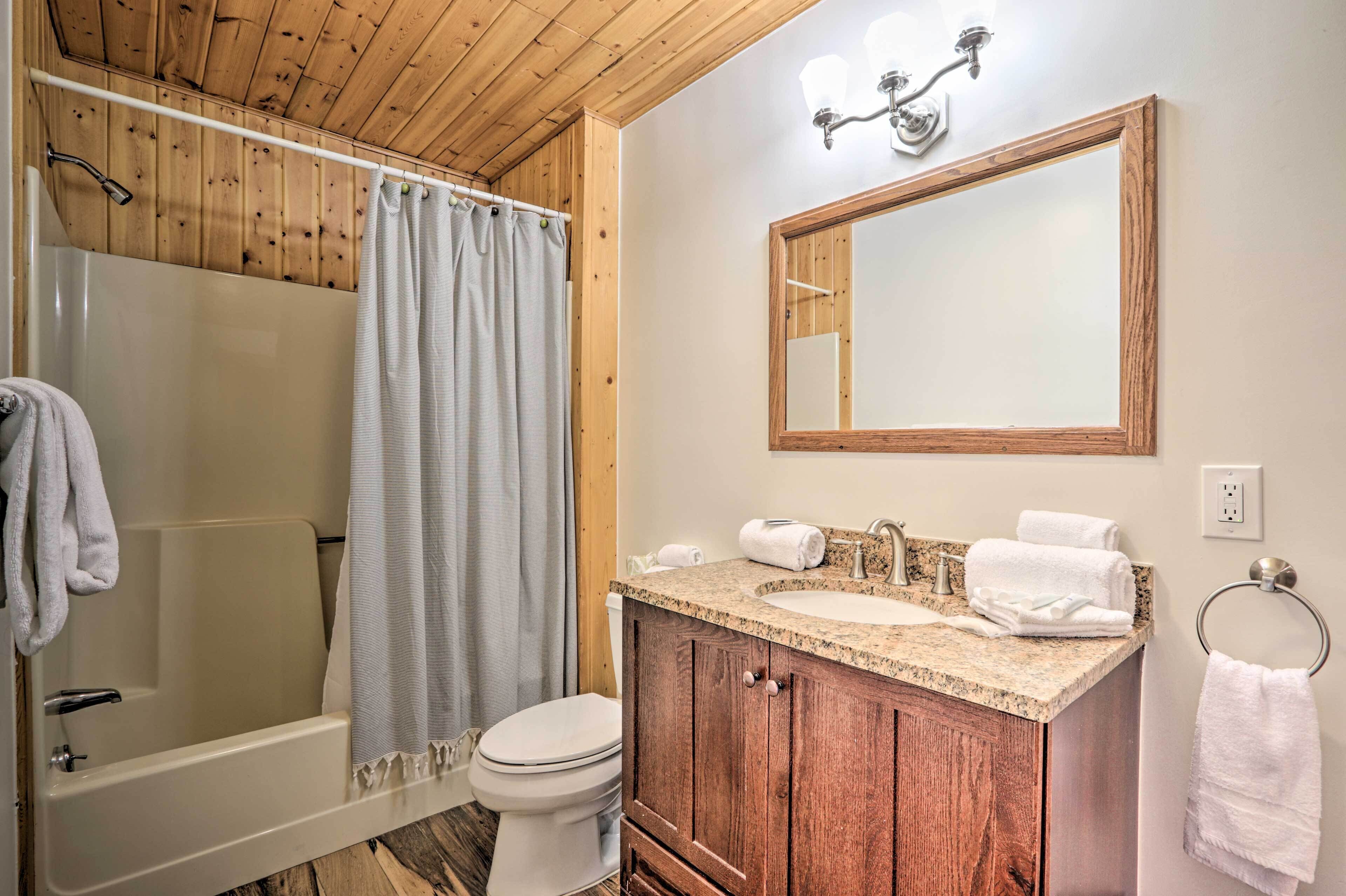 A bathroom with a wooden ceiling, a shower, a toilet, a sink with a vanity, and a mirror.