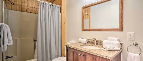 A bathroom with a wooden ceiling, a shower, a toilet, a sink with a vanity, and a mirror.