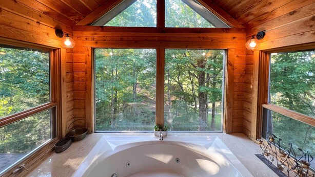 A wooden cabin with a large bathtub and windows overlooking a forest. - Deck & Hot Tub: Mtn-view Gatlinburg Cabin (Gatlinburg)