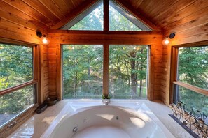 A wooden cabin with a large bathtub and windows overlooking a forest. - Deck & Hot Tub: Mtn-view Gatlinburg Cabin (Gatlinburg)