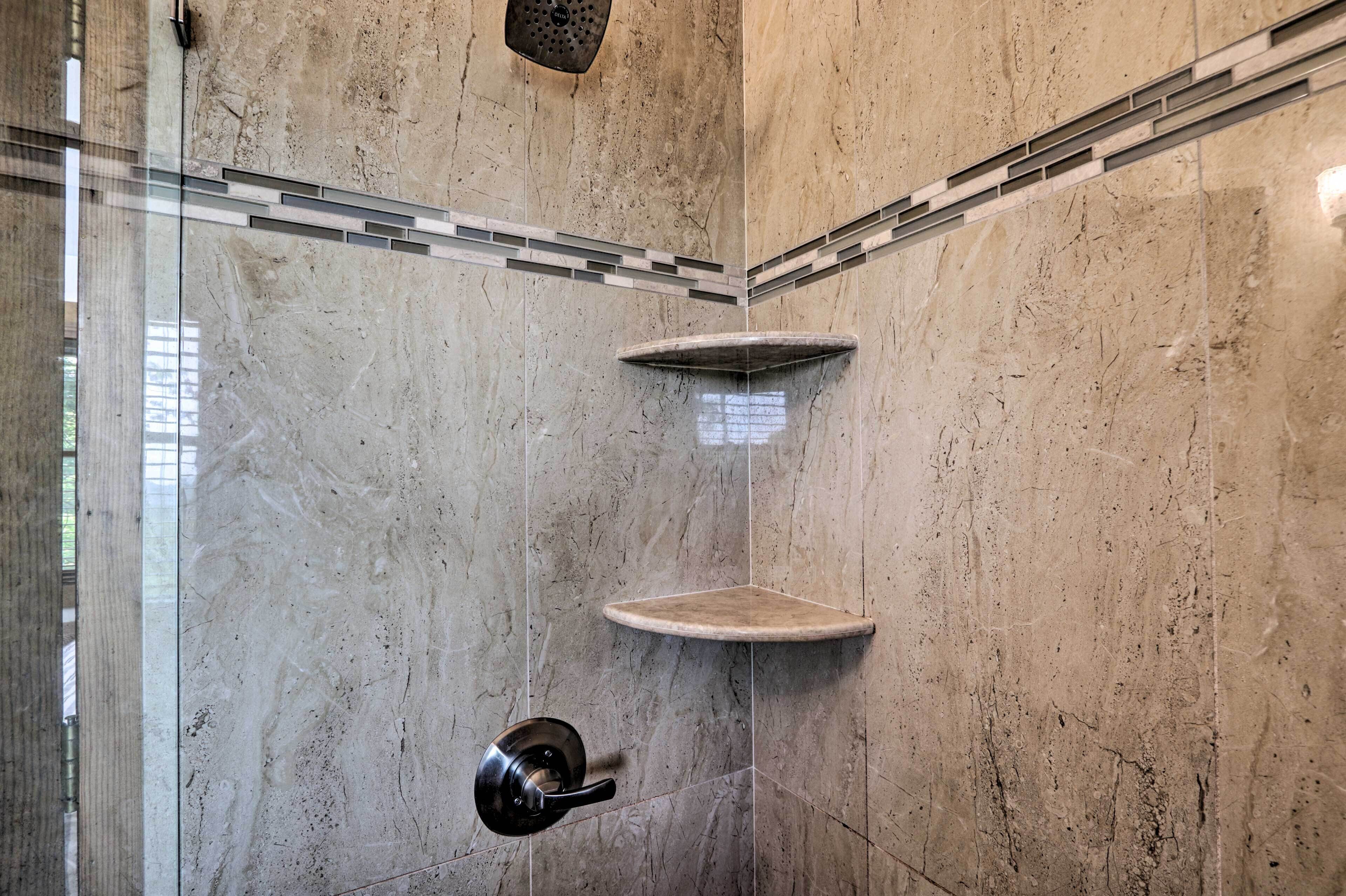 Un espacio de ducha moderno con puerta de cristal, pared de mármol y repisa en esquina.
