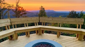 A wooden deck with a built-in fire pit and a bench, overlooking a mountainous landscape during sunset. - Deck & Hot Tub: Mtn-view Gatlinburg Cabin (Gatlinburg)