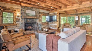 A cozy living room with a stone fireplace, leather sofas, and a large TV. - Deck & Hot Tub: Mtn-view Gatlinburg Cabin (Gatlinburg)