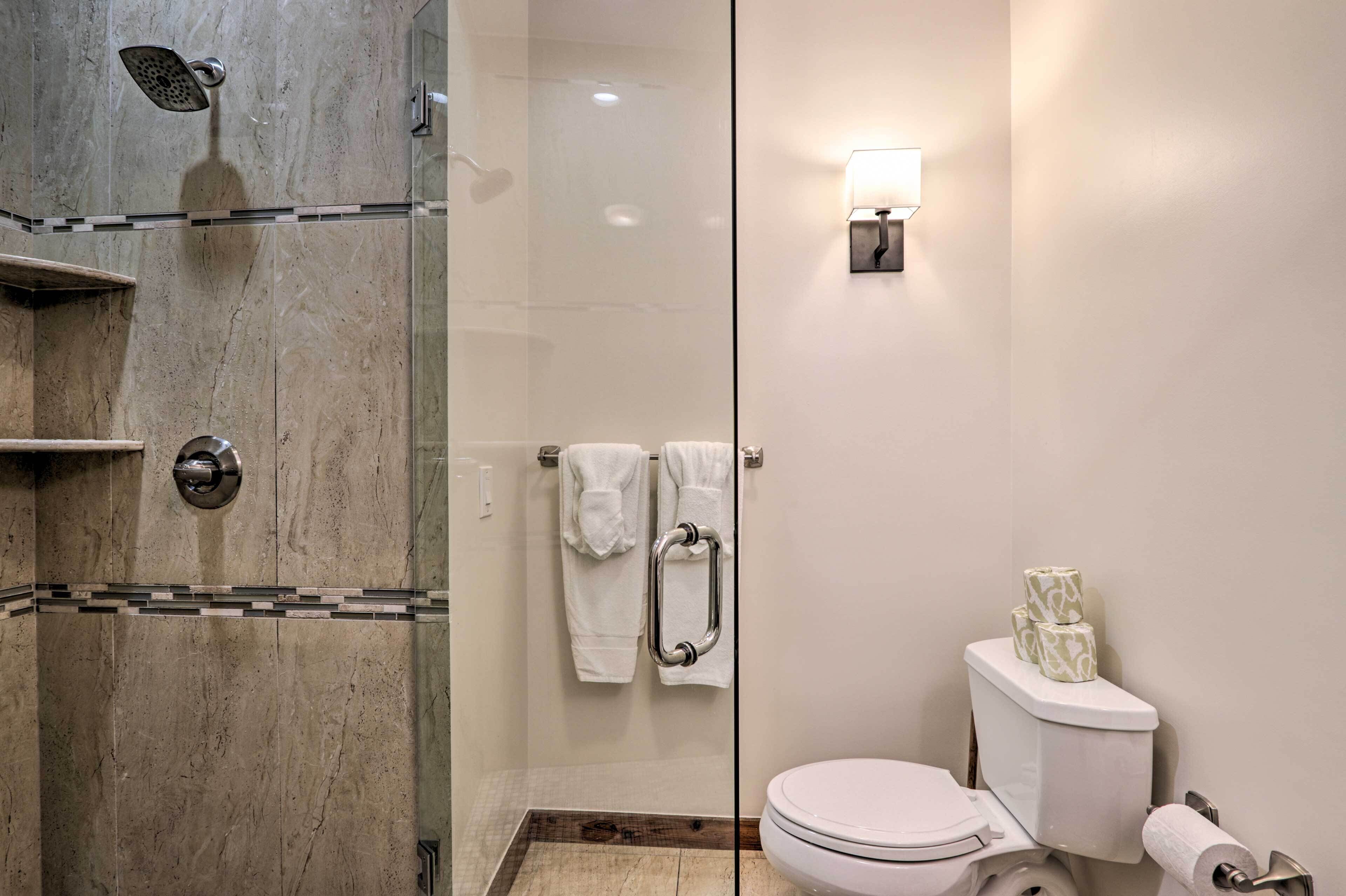 Un baño moderno con ducha de vidrio, inodoro con papel higiénico y toallas de papel, y un aplique de pared.
