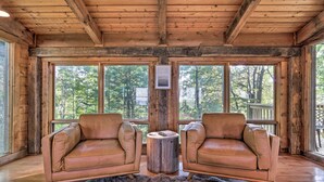 A cabin interior with two leather sofas facing a wooden table, large windows offering a view of the forest, and a wooden ceiling. - Deck & Hot Tub: Mtn-view Gatlinburg Cabin (Gatlinburg)