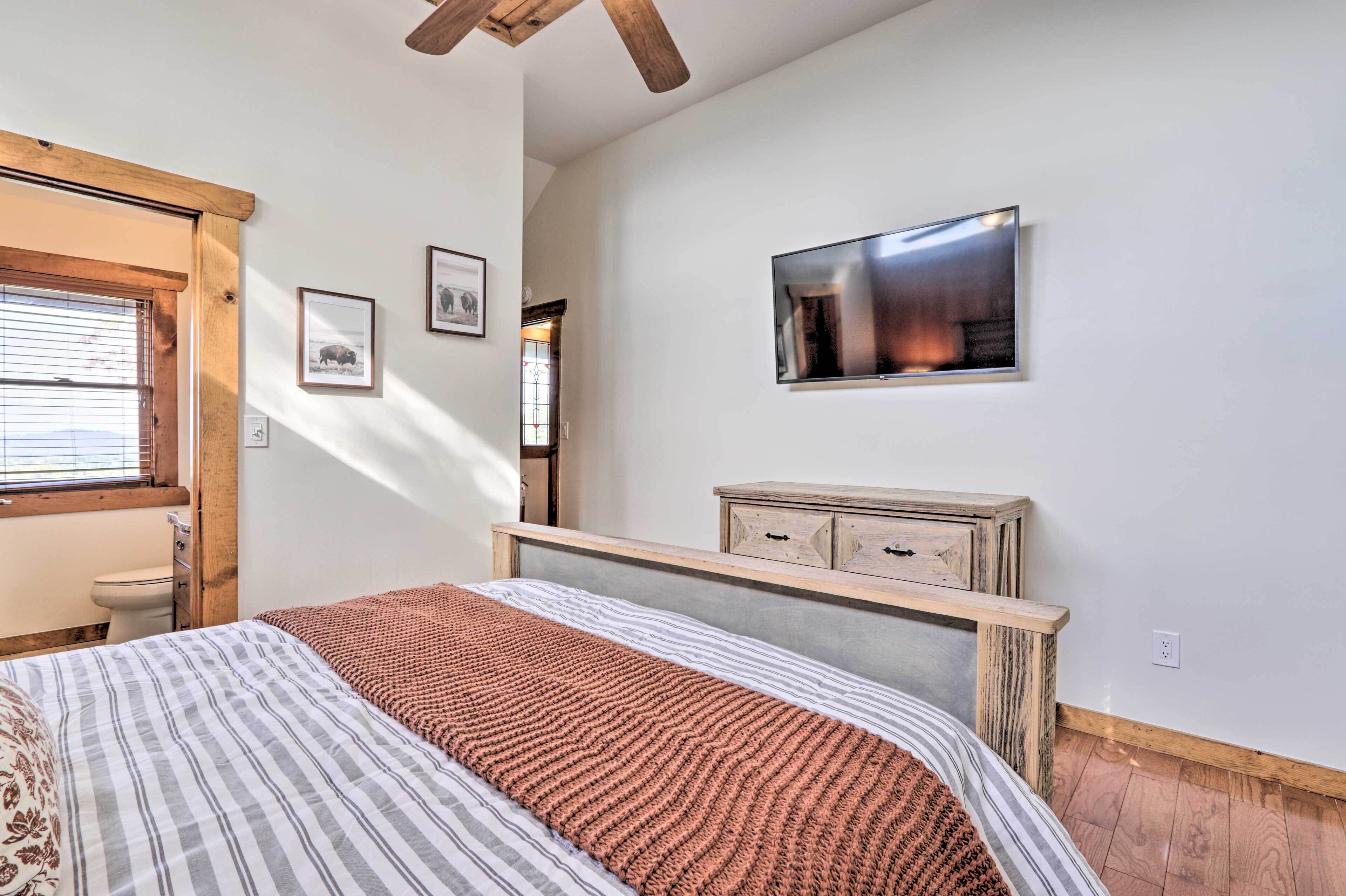 A bedroom with a bed, a wooden headboard, a TV mounted on the wall, and a window with blinds.
