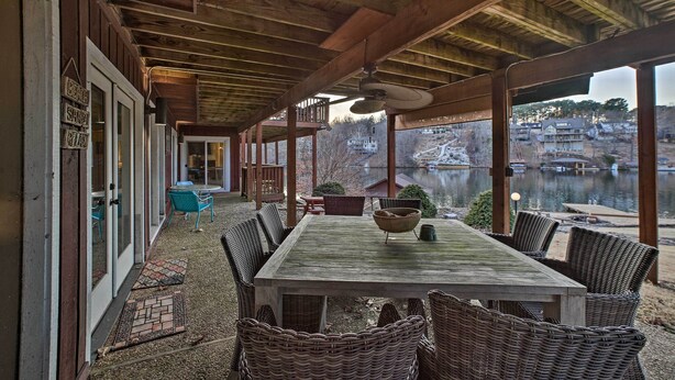 A covered outdoor dining area with a table and wicker chairs, overlooking a body of water and buildings. - Lakefront Retreat w/ Dock & Beach: 2 Miles to Golf (Bella Vista)