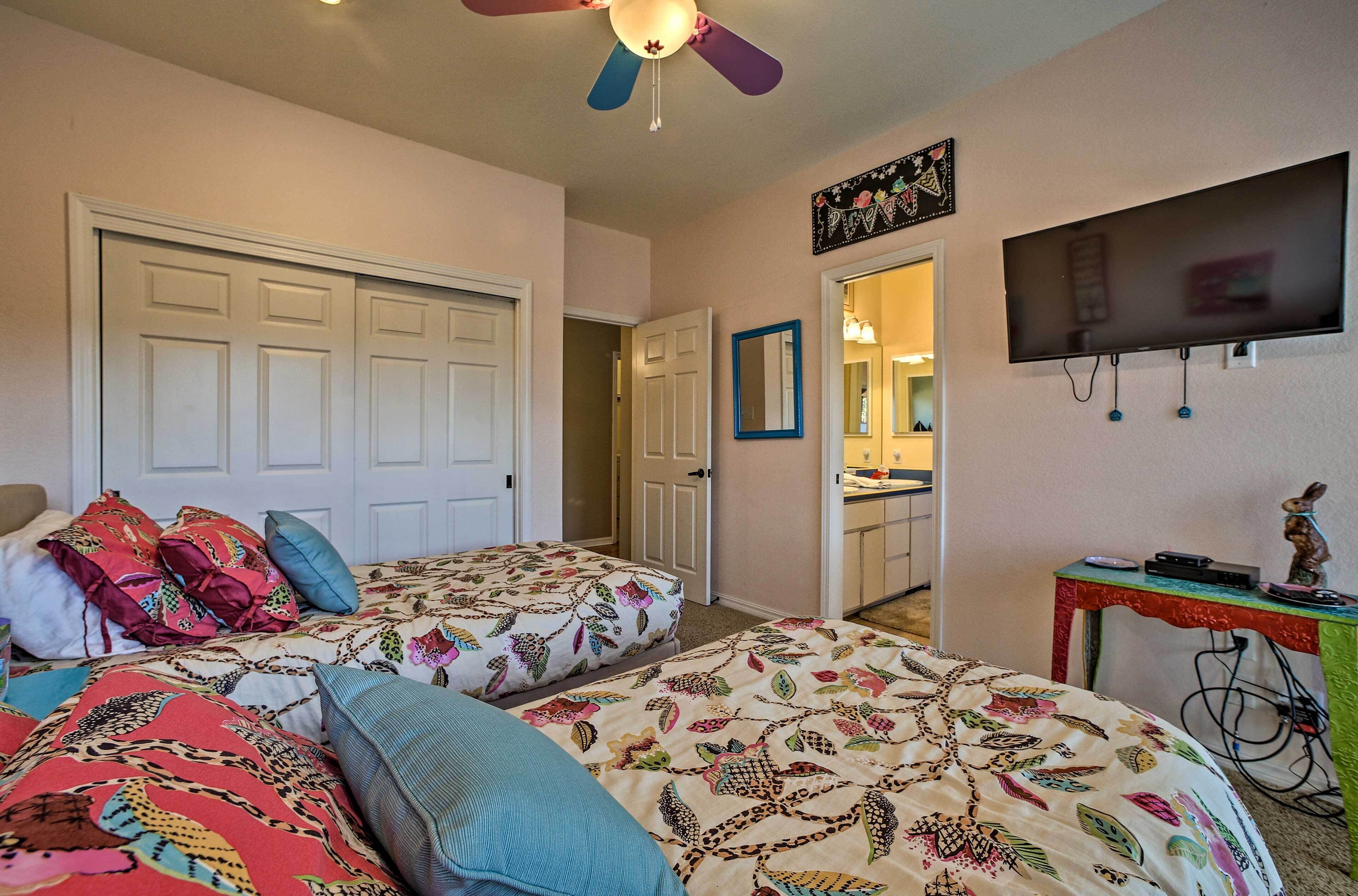 A bedroom with two beds, a ceiling fan, a TV, and a small table with a statue.
