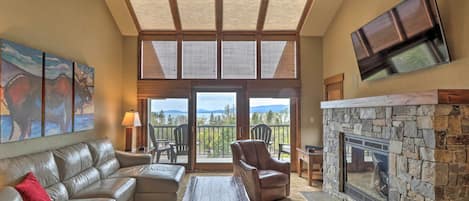 A spacious living room with a stone fireplace, leather sofas, a wooden coffee table, and a large window overlooking a scenic view.