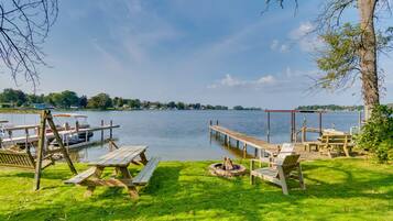 A lakeside picnic area with wooden benches, picnic tables, and a fire pit.