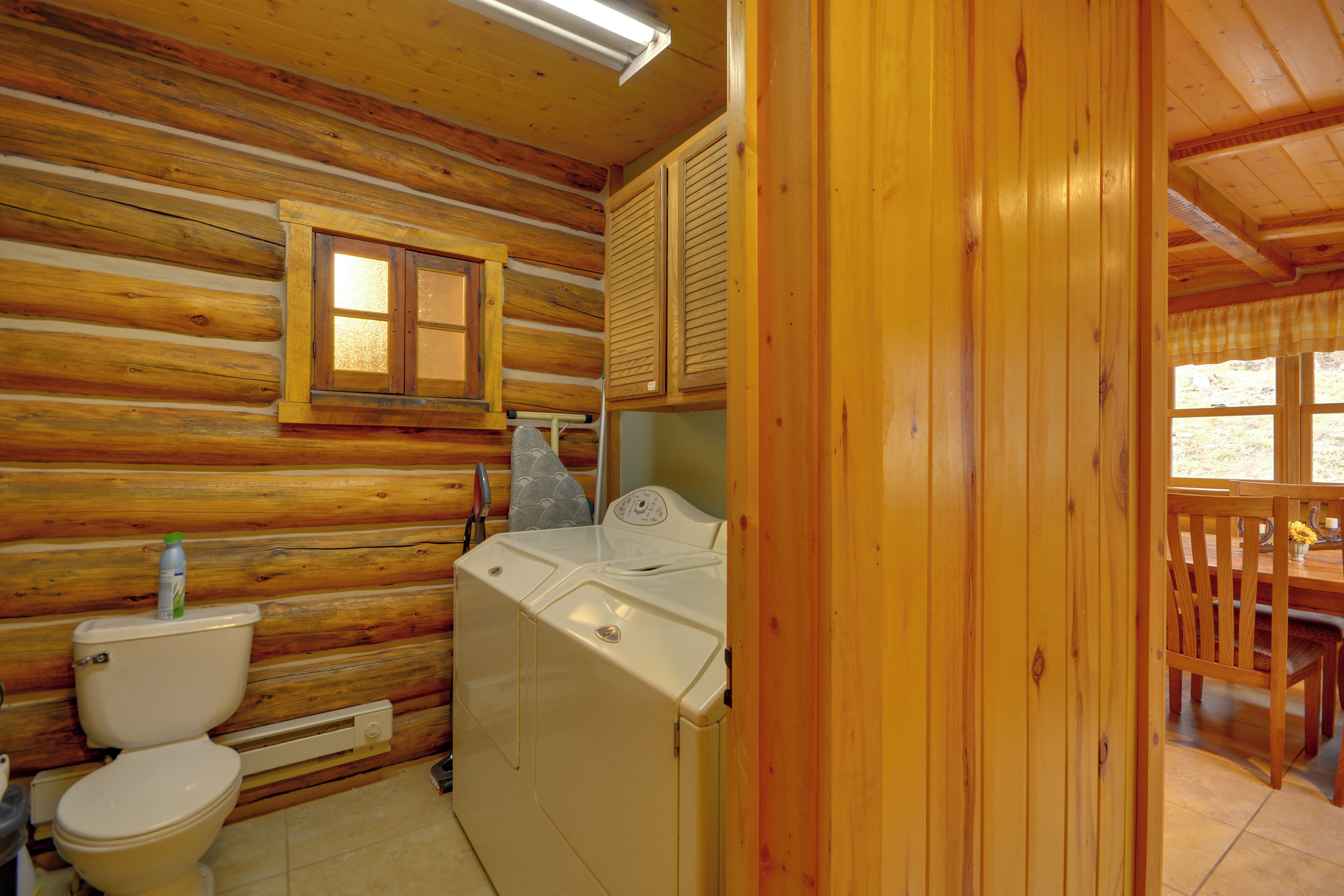 A wooden cabin interior with a toilet, washing machine, and a small window.