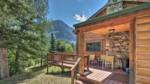 A log cabin with a deck, outdoor seating, and a stone fireplace. - 'honey's Cabin' in Mcleod: Fish, Hike & Views! (McLeod)