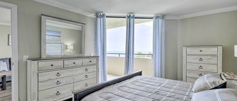 A bedroom with a large bed, a dresser, a mirror, and a view of the outdoors through a window.