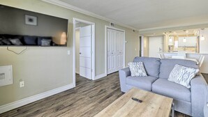 A living room with a grey sofa, a wooden coffee table, and a TV mounted on the wall. - Waterfront Resort Condo w/ Private Beach & Pool (Hudson)