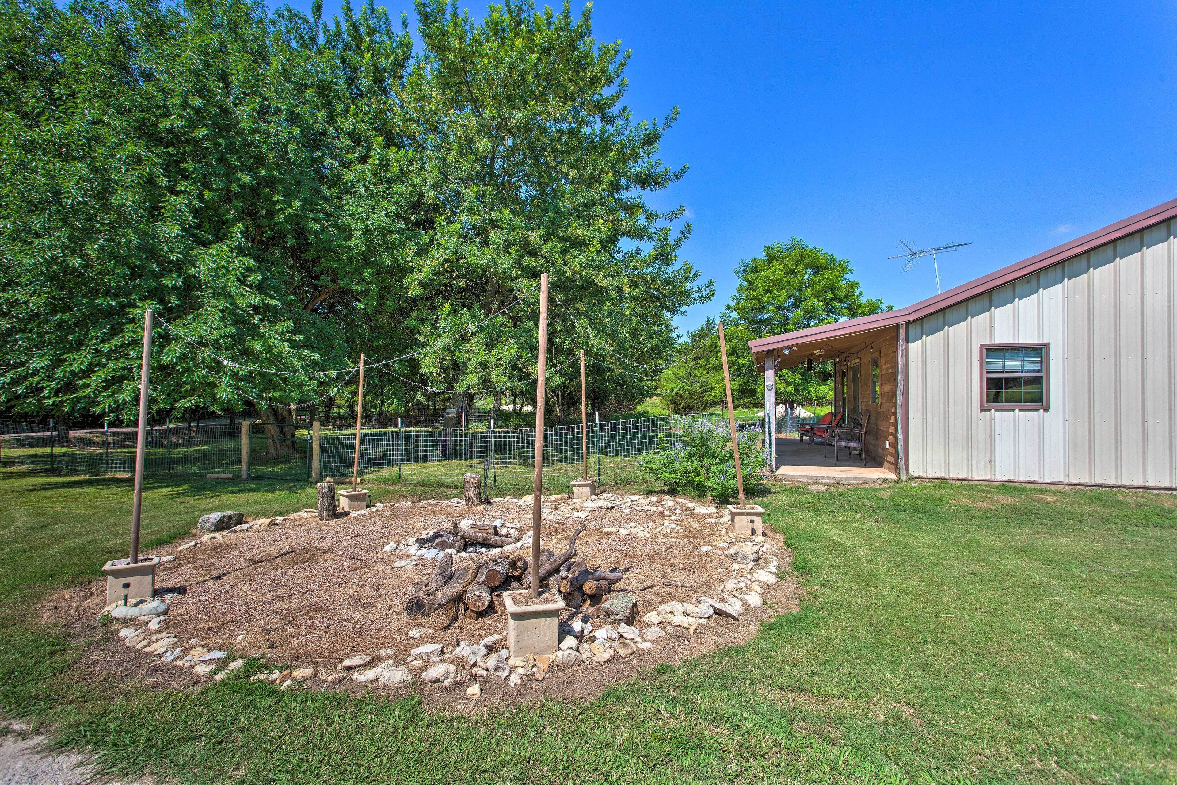 A fenced outdoor area with a fire pit, a wooden structure, and a building with a red roof.