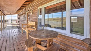 A wooden log cabin with a covered porch, a round wooden table, and large windows offering a view of the landscape. - Secluded Belle Fourche Cabin: Group Friendly! (Belle Fourche)