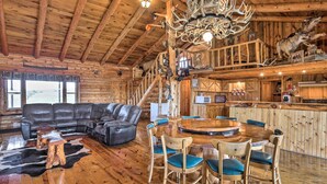 A log cabin interior with a wooden dining table, chairs, a leather sofa, and a chandelier. - Secluded Belle Fourche Cabin: Group Friendly! (Belle Fourche)