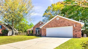 A single-story brick house with a garage, a front yard, and a tree with yellow leaves. - Ocean Springs Home w/ Fire Pit & Game Room! (Biloxi)