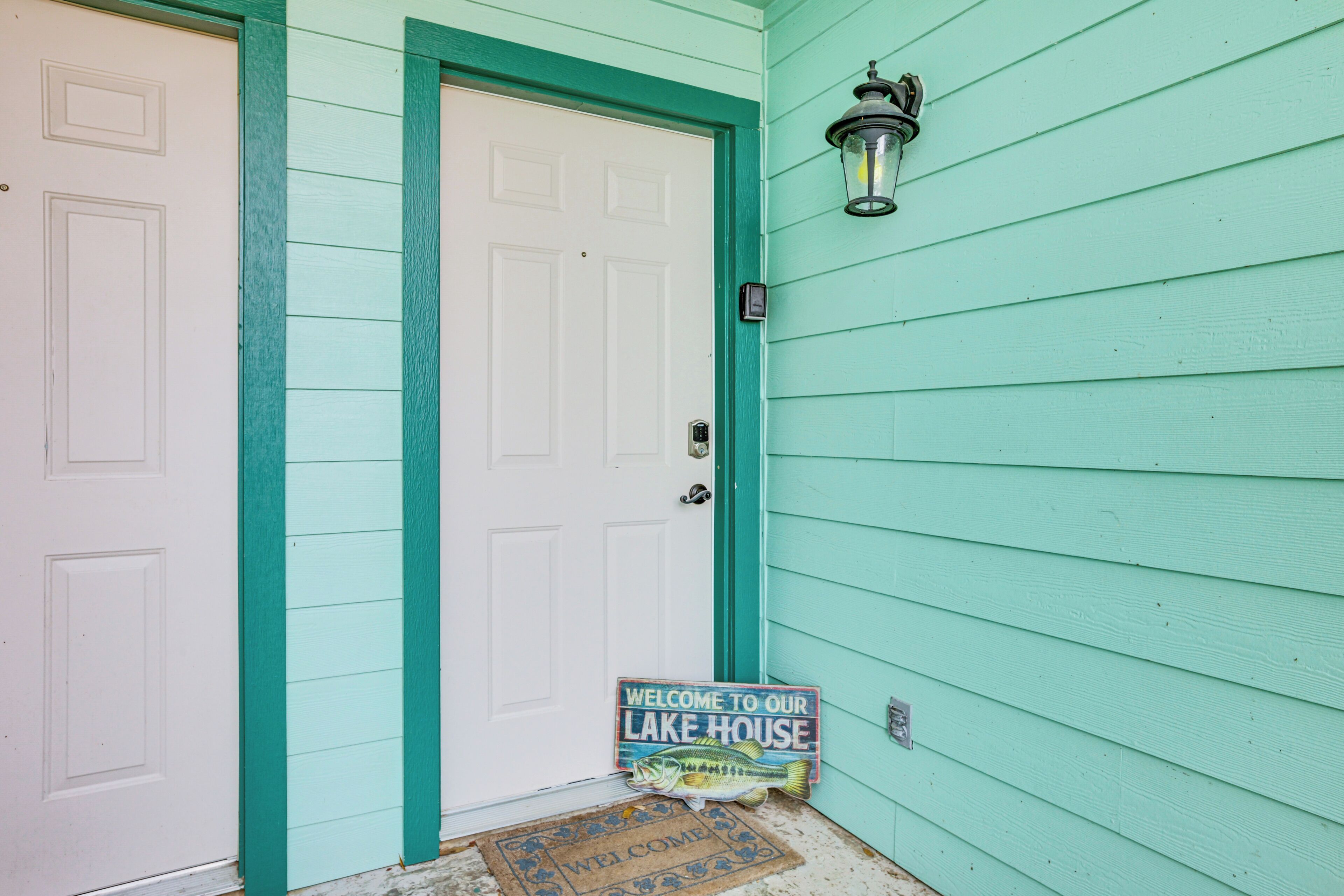 Une maison avec une porte blanche et des moulures turquoise, une pancarte indiquant « Bienvenue » et une enseigne représentant un poisson.