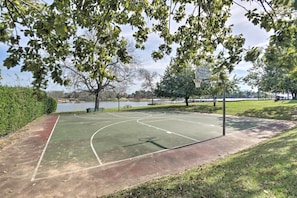 An outdoor basketball court with a net, surrounded by trees and a body of water in the background. - Resort-style Lake Conroe Retreat w/ Balcony & View (Willis)