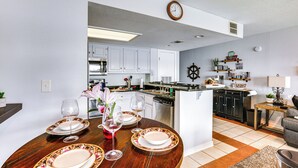 A modern kitchen with white cabinets, a central island, and a dining area set with floral tableware and wine glasses. - Resort-style Lake Conroe Retreat w/ Balcony & View (Willis)